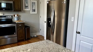 A kitchen with granite countertops, stainless steel appliances, wooden cabinets, and framed artwork on the wall. - Beach Cottage/2 pools/Golf Cart Friendly/Beach Access (Gulf Shores)