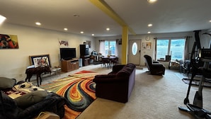 A living room with a large TV, a sofa, a colorful rug, and a treadmill.