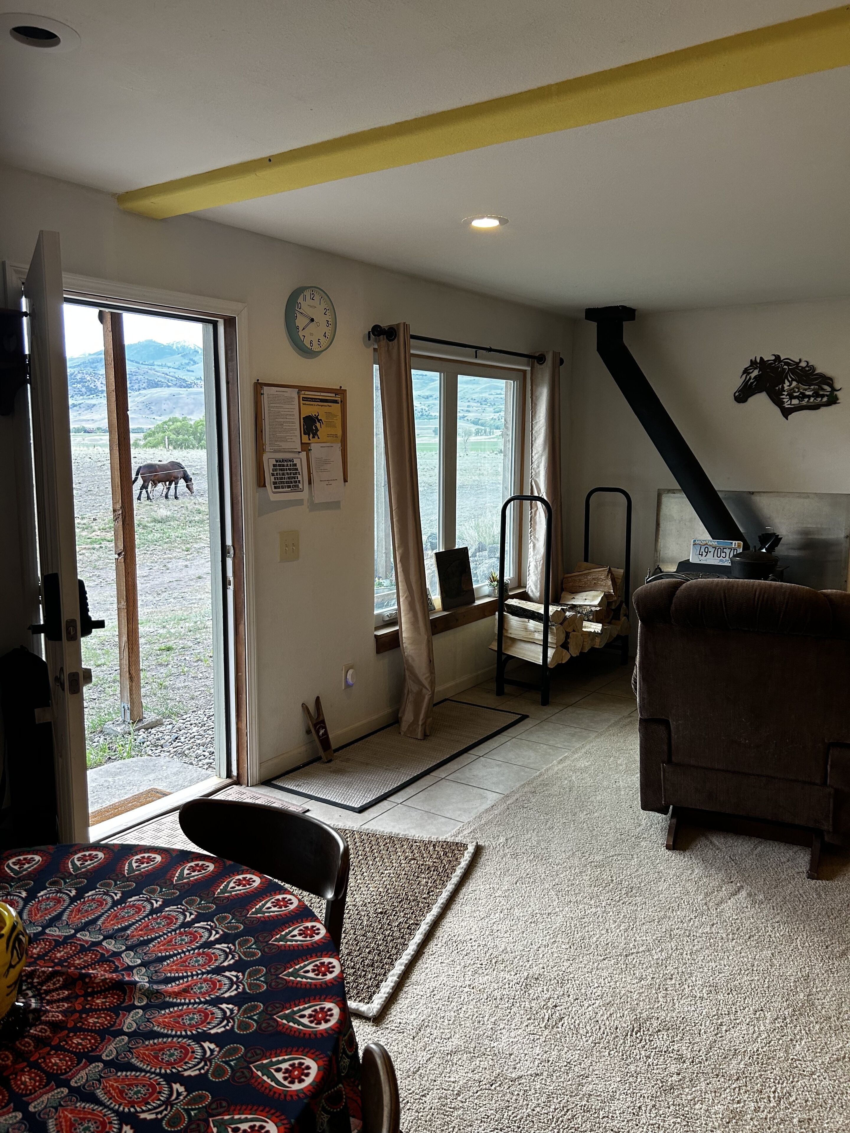 A room with a door leading to a balcony, a clock on the wall, a sofa, and a patterned rug.