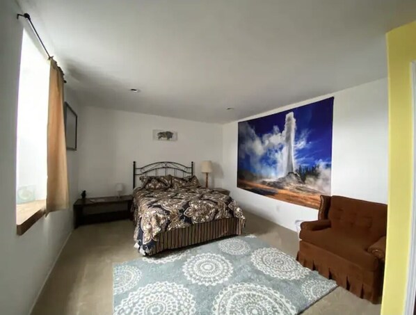 A bedroom with a bed, a painting, a chair, and a window with curtains.