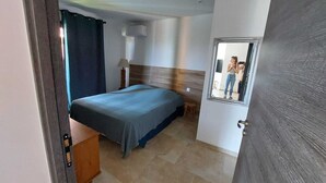 Un dormitorio con cama, mesita de noche, lámpara y espejo en la pared.