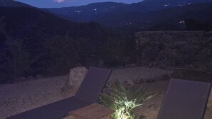 Dos sillones de descanso mirando un paisaje rocoso con vistas a colinas distantes y una planta pequeña iluminada.