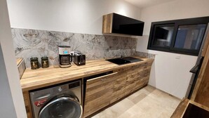 Cocina pequeña con cafetera, tostadora y tarros de té en la encimera, lavadora y ventana sobre el lavabo.