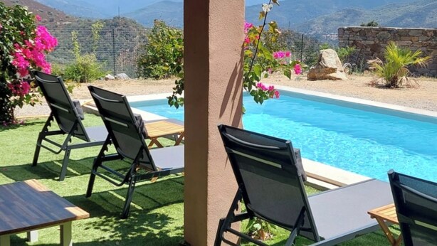 Zona junto a la piscina con césped artificial, sillas de descanso y vistas a montañas.