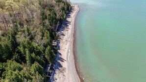 An aerial view of a beach with a wooden structure near the water's edge, surrounded by dense trees.