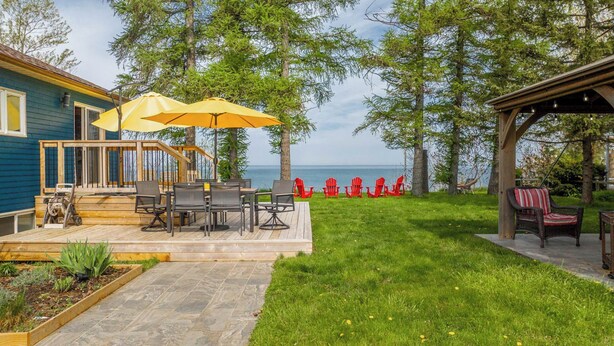 A deck with outdoor furniture and a yellow umbrella, overlooking a grassy area and a body of water. - Sunset at SchadeView, Lake views, King Bed (Dashwood)