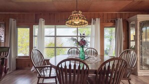 A wooden-paneled dining room with a round table, six chairs, and a hanging light fixture. - Sunset at SchadeView, Lake views, King Bed (Dashwood)