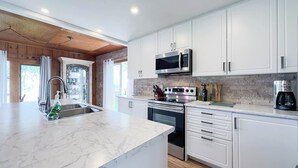 A modern kitchen with white cabinets, a marble countertop, stainless steel appliances, and a large window. - Sunset at SchadeView, Lake views, King Bed (Dashwood)