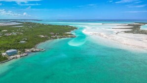 Vue aérienne d’une zone côtière avec des eaux turquoise limpides, une petite île dotée de bâtiments et une jetée.
