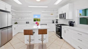 Une cuisine moderne avec des meubles blancs, des appareils en acier inoxydable, un îlot central doté de tabourets et une grande fenêtre offrant une belle vue.