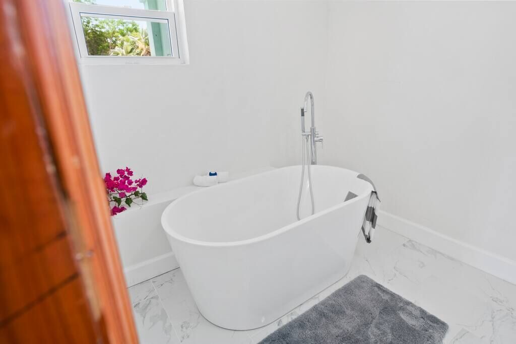 A modern bathroom with a freestanding bathtub, a small window, and a decorative flower arrangement.