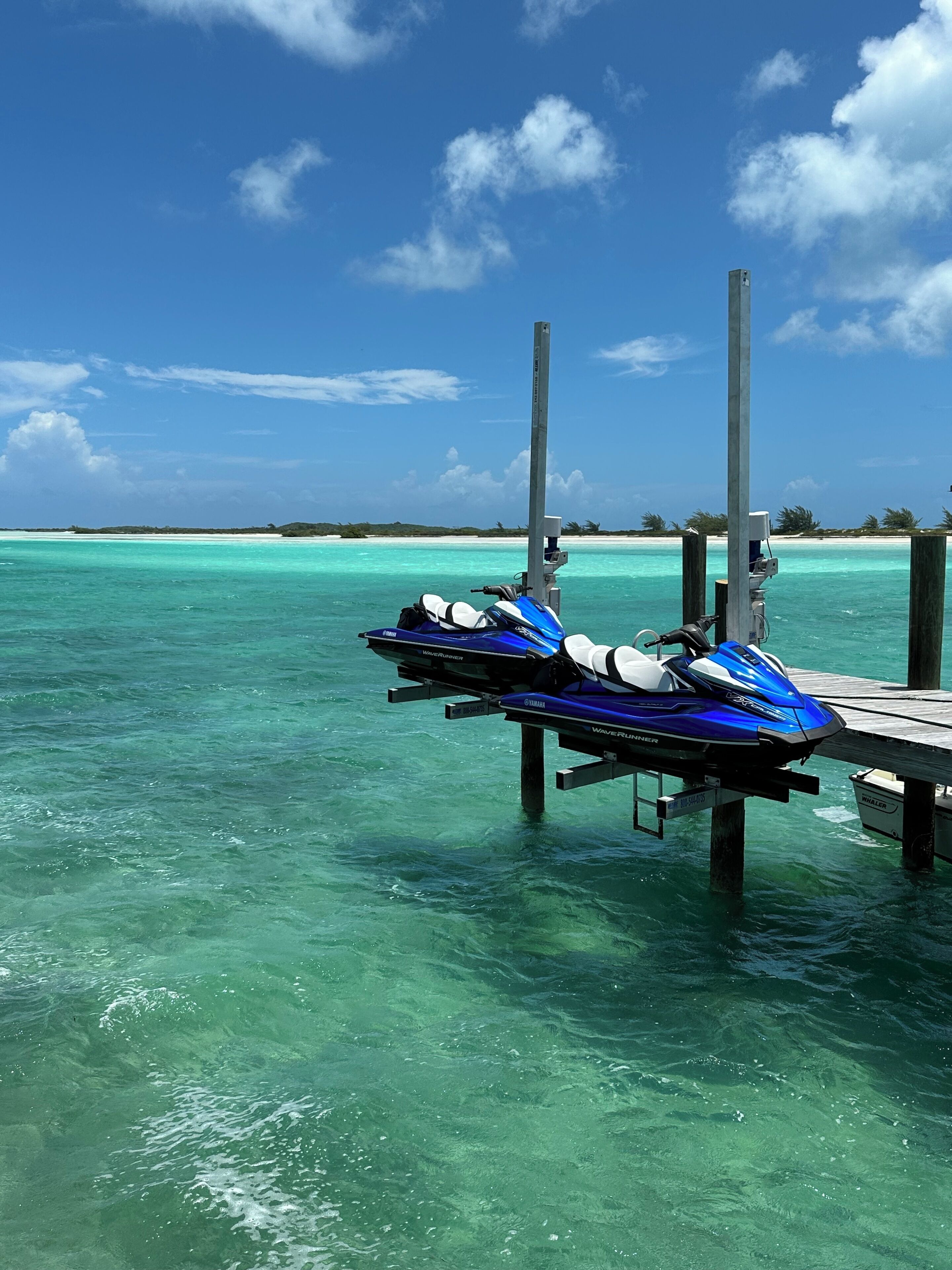 A pier with jet skis docked, clear turquoise water, and a distant shoreline with vegetation.