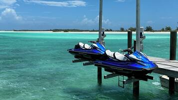 A pier with jet skis docked, clear turquoise water, and a distant shoreline with vegetation.