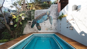 A swimming pool with a mural of a sea turtle on the wall, surrounded by wooden decking and greenery.