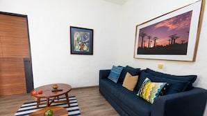 A living room with a sofa, a coffee table, a framed abstract painting, and a landscape painting.