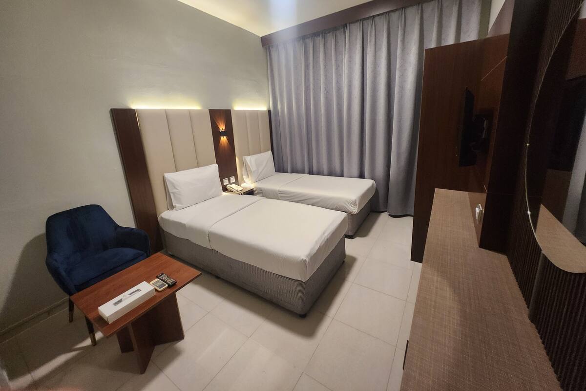 A hotel room with two beds, a desk, a chair, and a large window with curtains.