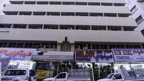 Un edificio de varios pisos con fachada plana, varios balcones y locales comerciales, incluyendo tiendas de muebles.