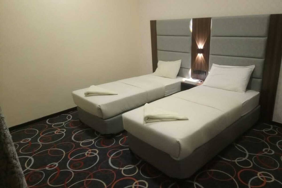 A hotel room with two single beds, a headboard with integrated lighting, and a patterned carpet.