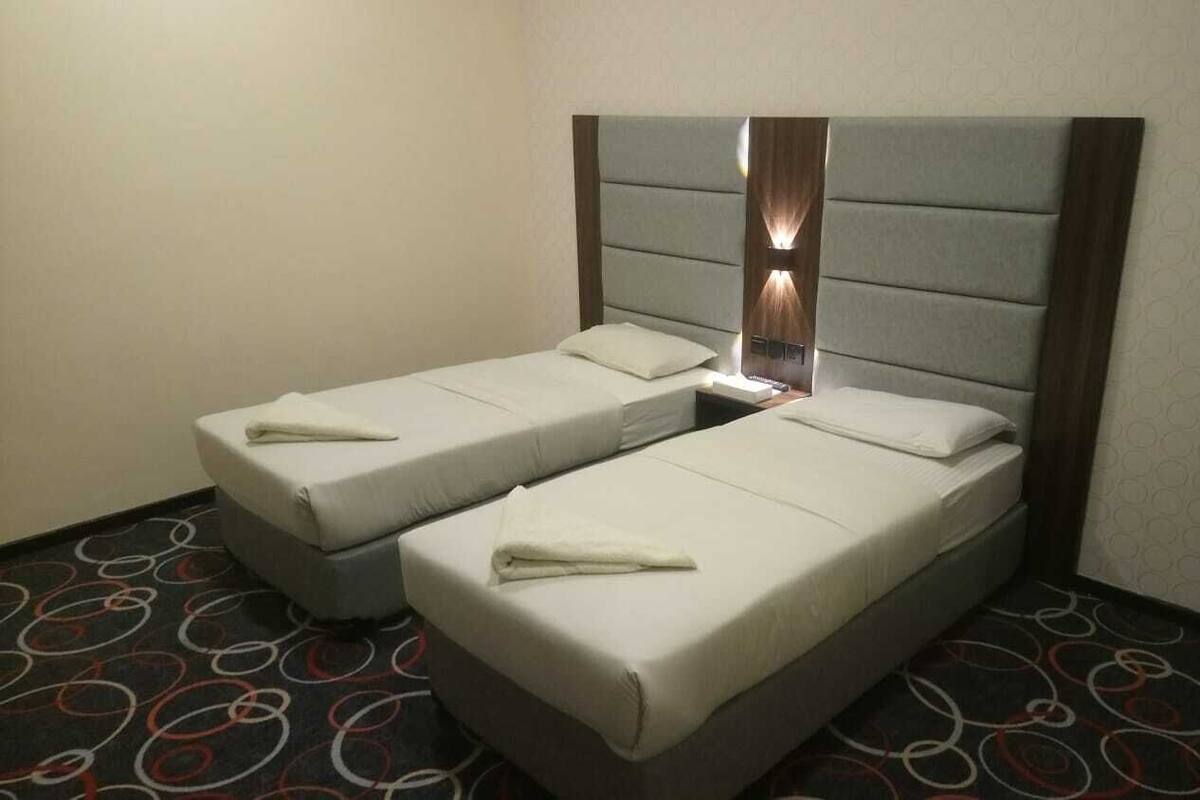 A hotel room with two single beds, a nightstand, and a wall-mounted lamp.