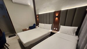 Habitación de hotel con dos camas individuales, una mesita de noche, una silla y aire acondicionado de pared.
