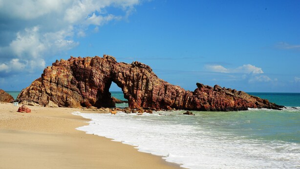 A beach with a large rock formation featuring an arch. - Pousada Canaã (Jijoca de Jericoacoara)