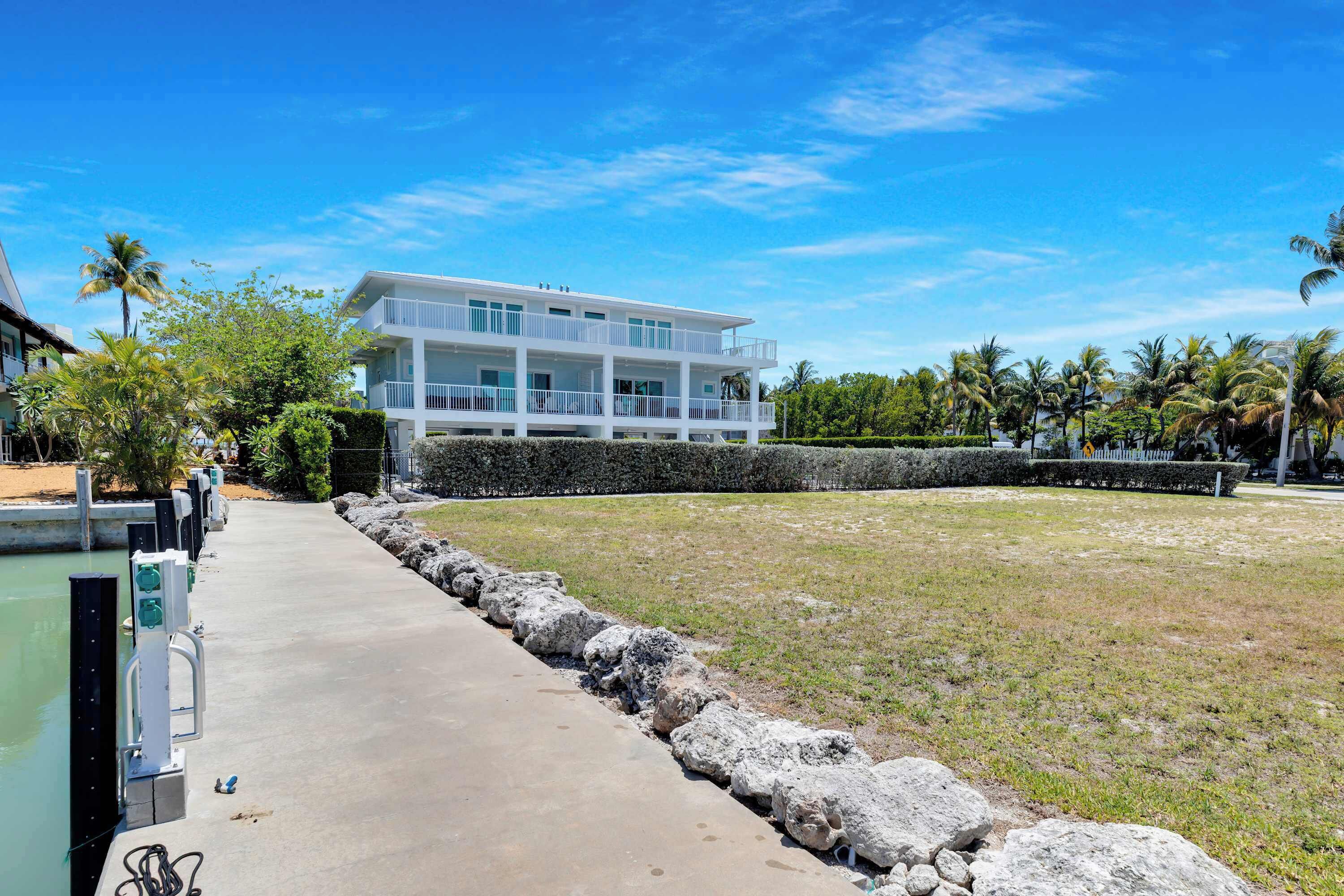 A modern two-story building with a balcony, surrounded by a well-maintained lawn and palm trees.