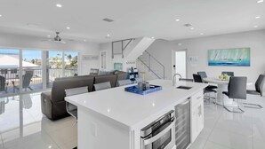 A modern kitchen with a central island, a dining area with a table and chairs, a staircase, and a view of the outdoors. - Cielo's Del Mar 1 - Pool/Dock/Beach Luxury in KCB (Key Colony Beach)