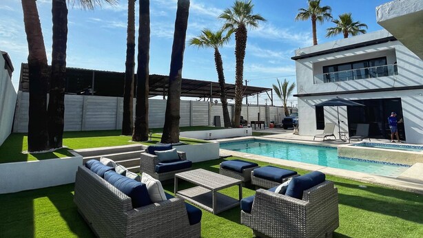 A pool area with artificial grass, wicker lounge chairs, and palm trees.