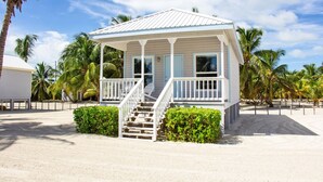 A beach house with a covered porch, a staircase, and a sandy beach in the background.