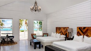 A room with two beds, a chandelier, a table with chairs, and a view of the beach.