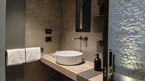 Un baño moderno con un lavabo redondo, un espejo y una pared con textura.