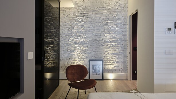 Un dormitorio moderno con una pared de acento de piedra, un cuadro enmarcado y una silla marrón.
