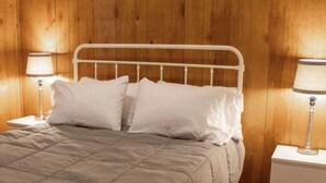 A bed with a white metal frame and a beige quilted bedspread. There are two bedside lamps with white shades on either side of the bed.