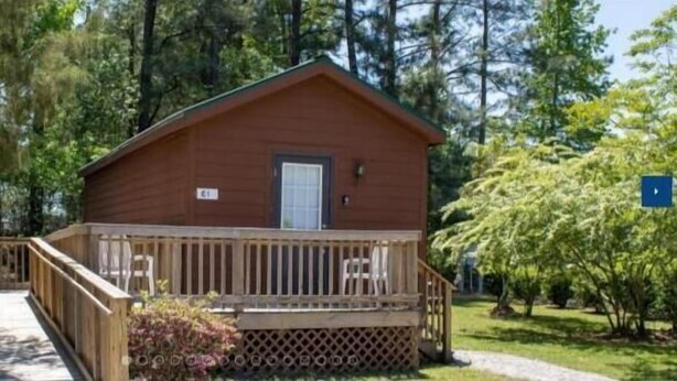 A wooden cabin with a porch and a small deck, surrounded by trees.