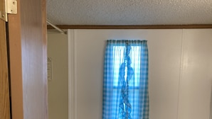 Een badkamer met een toilet, een toiletrol op een houder, een raam met een blauw geruit gordijn en een houten deur.