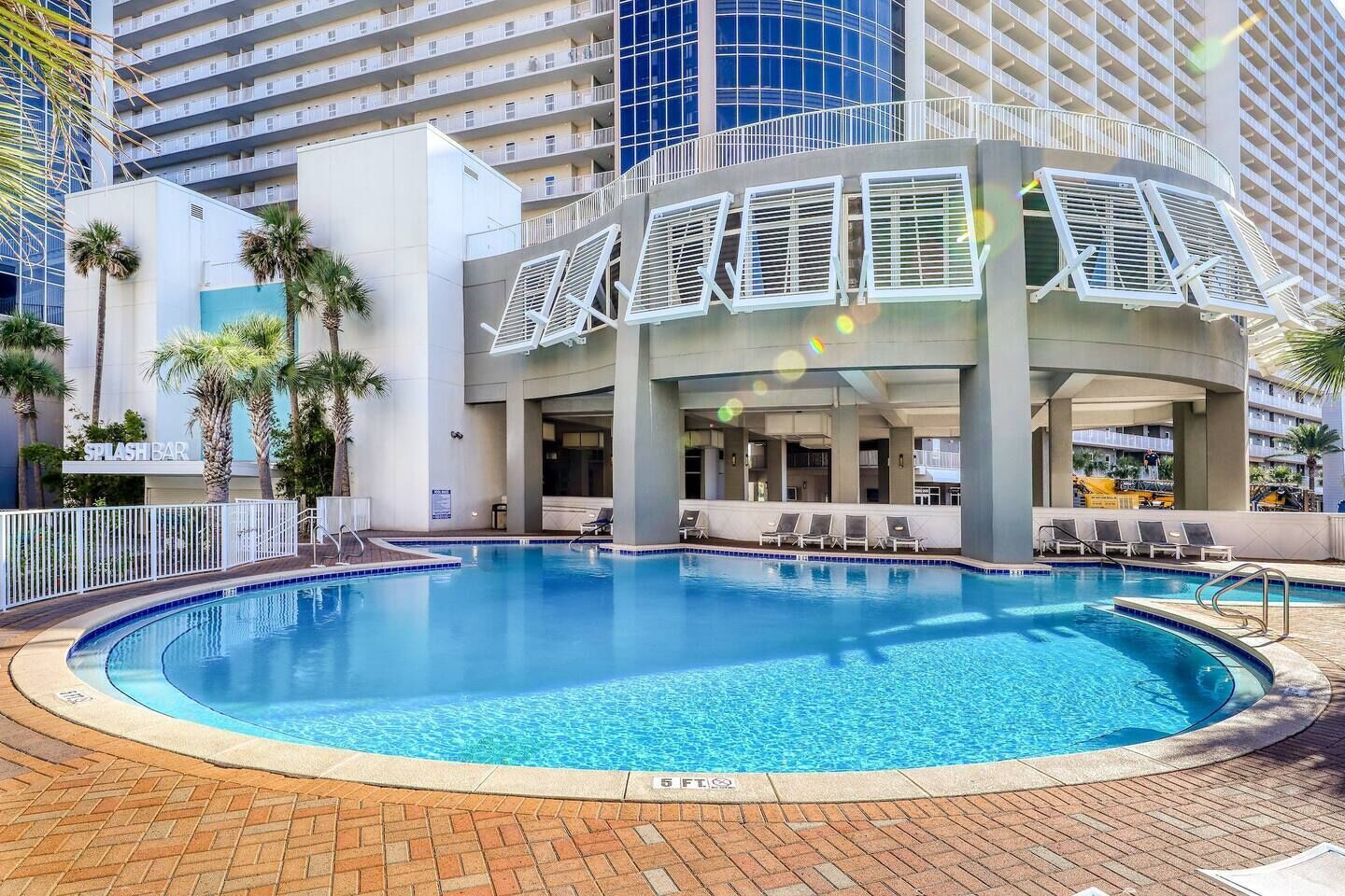 A swimming pool with lounge chairs, a bar, and a view of a high-rise building.