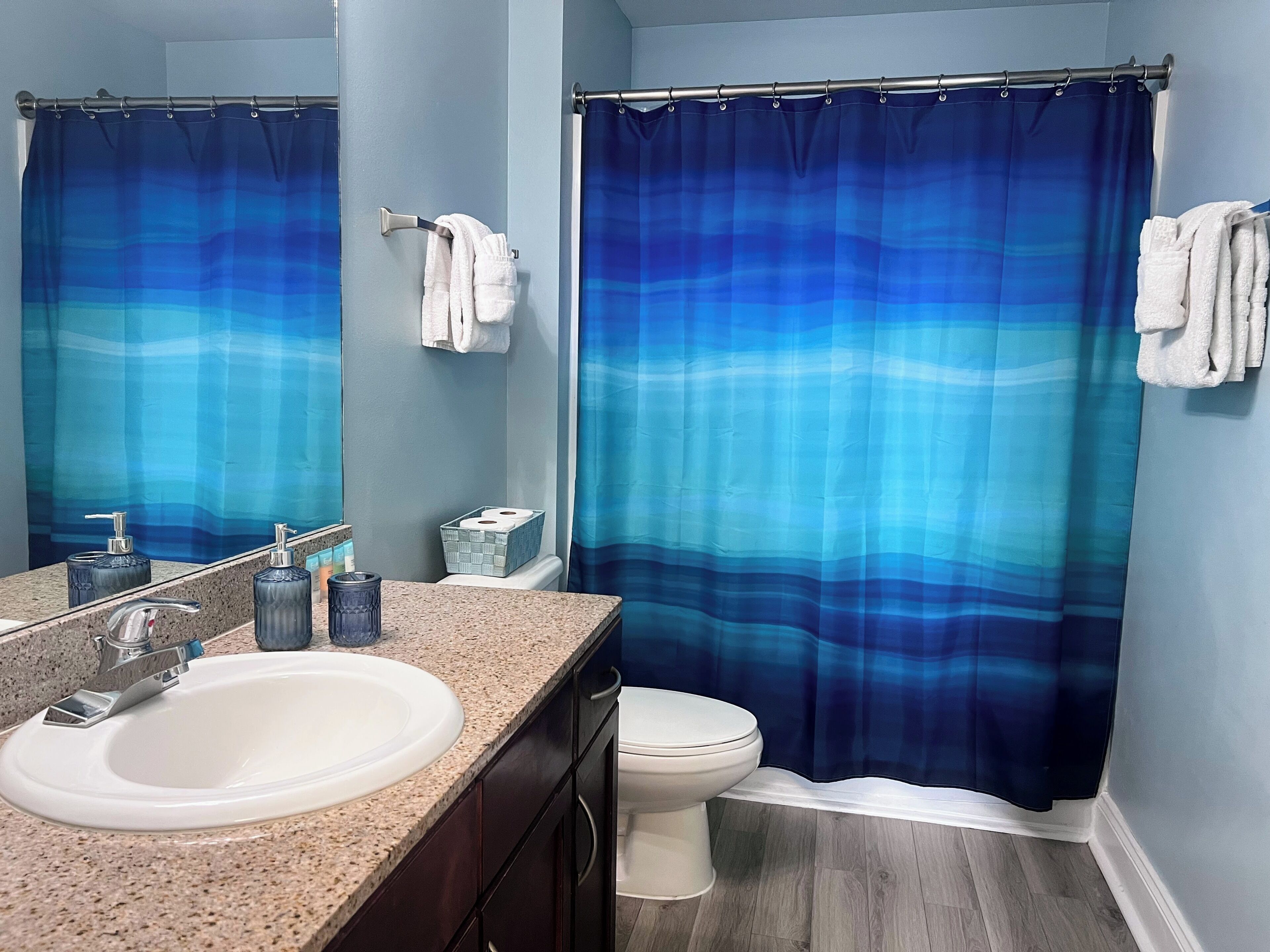 Une salle de bain avec un lavabo blanc, des toilettes et un rideau de douche bleu dégradé.