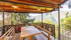 Un espace extérieur abrité, aménagé avec une table en bois et des bancs, entouré de rampes en métal décoratives ornées d’écussons héraldiques.