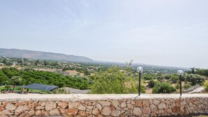 A stone wall with a view of a rural landscape, including trees, a hill, and a clear sky. - Cozy home in Floridia (Floridia)