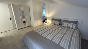 A bedroom with a bed, a bedside table, a wardrobe, and a mirror. - Oasis Urbain (Argenteuil)