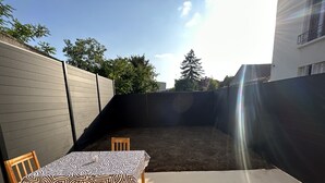 A backyard with a table and chairs, a wooden fence, and a building in the background. - Oasis Urbain (Argenteuil)