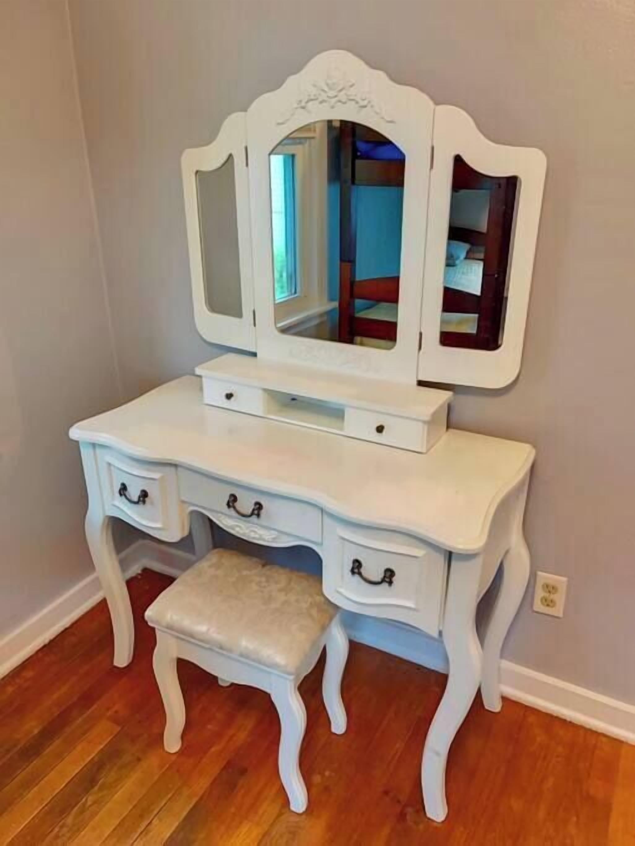 A white vanity with a mirror, drawers, and a stool.
