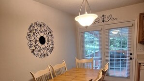 A dining area with a wooden table and chairs, a decorative wall piece, and a ceiling light fixture.