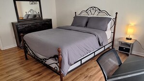 A bedroom with a bed, a desk, a chair, a ceiling fan, a dresser, and a wall sign.
