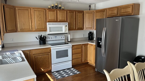 A kitchen with wooden cabinets, a white microwave, a stainless steel refrigerator, and a stove.