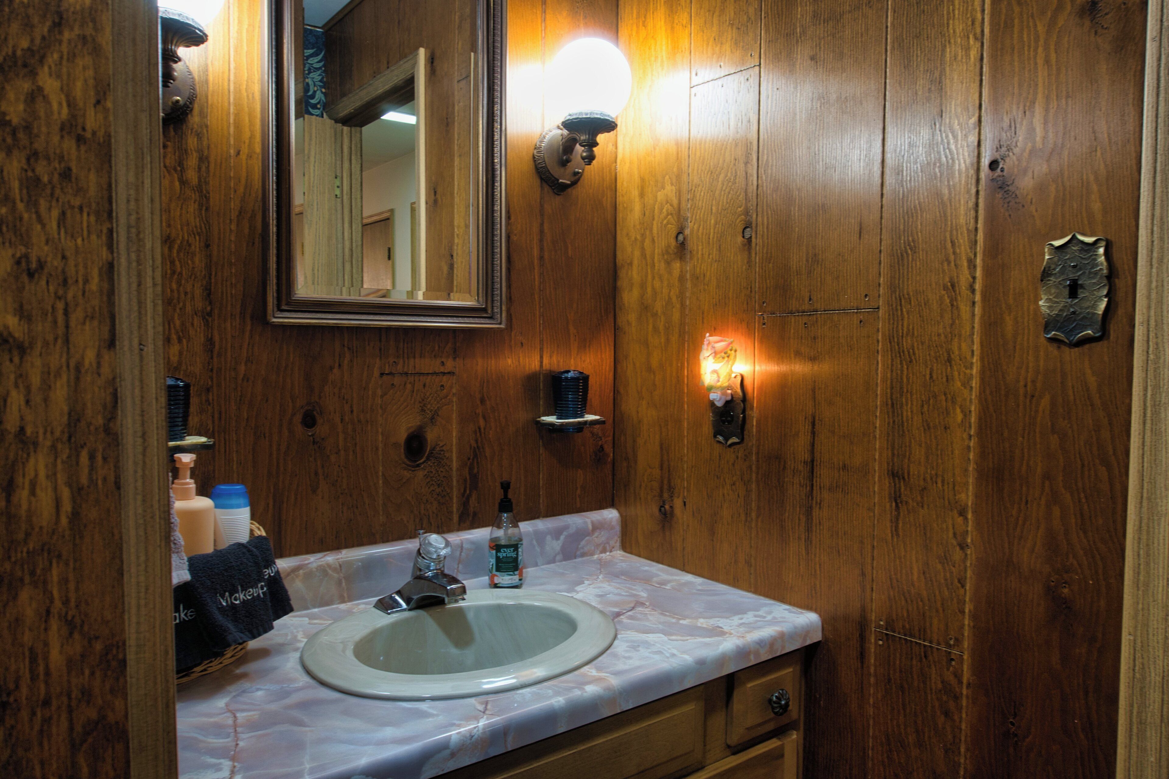 Une salle de bain avec un meuble-lavabo en bois, un évier, un miroir et un luminaire fixé au mur.