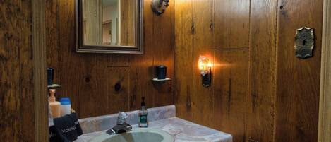 Une salle de bain avec un meuble-lavabo en bois, un évier, un miroir et un luminaire fixé au mur.