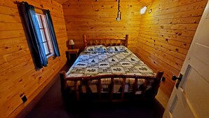 Ett mysigt rum i en stuga, inrett med träpanel, med en säng, ett fönster med gardiner och en dörr.
