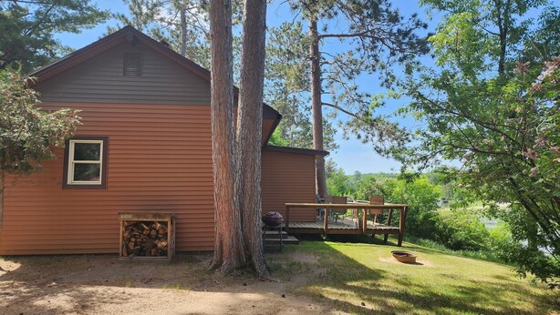En stuga med en veranda, omgiven av träd och en klar himmel.