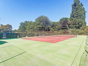 A tennis court with a red surface, surrounded by trees and a fence. - Studio de Charme ile D'oléron Piscine /tennis/terrain de Boules+ 700 m Plage (Dolus-d'Oléron)